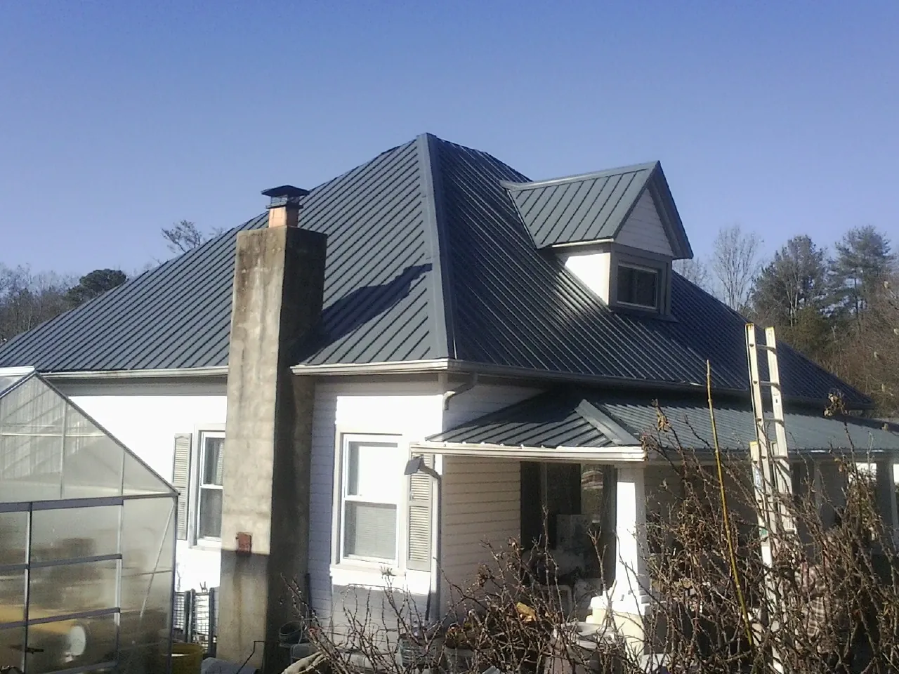 Dark blue standing seam metal roof on a white farmhouse with dormer — Slate & Tile Roof Repair by Roofing Brothers in Laurel