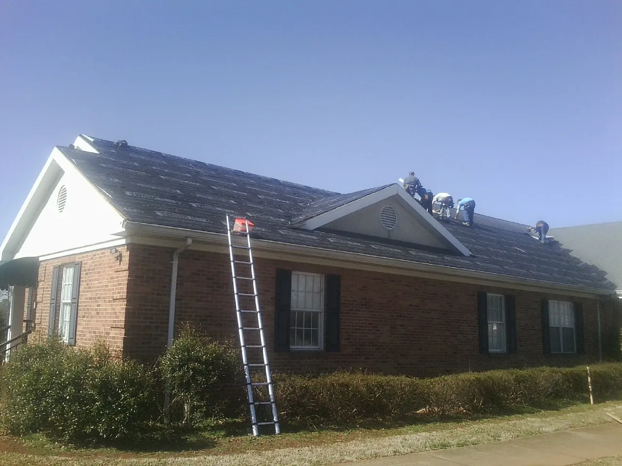 Crew tearing shingles off a brick ranch roof with a ladder set — Metal Roof Repair work by our crew in Laurel