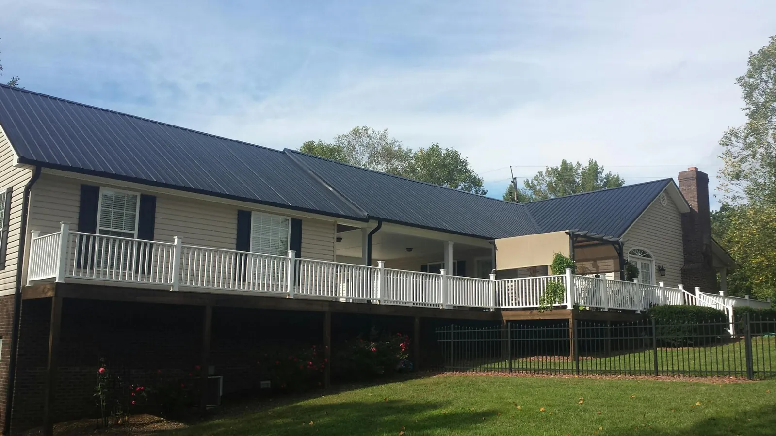 Black metal roof above a long white railed deck on a hillside home in Laurel