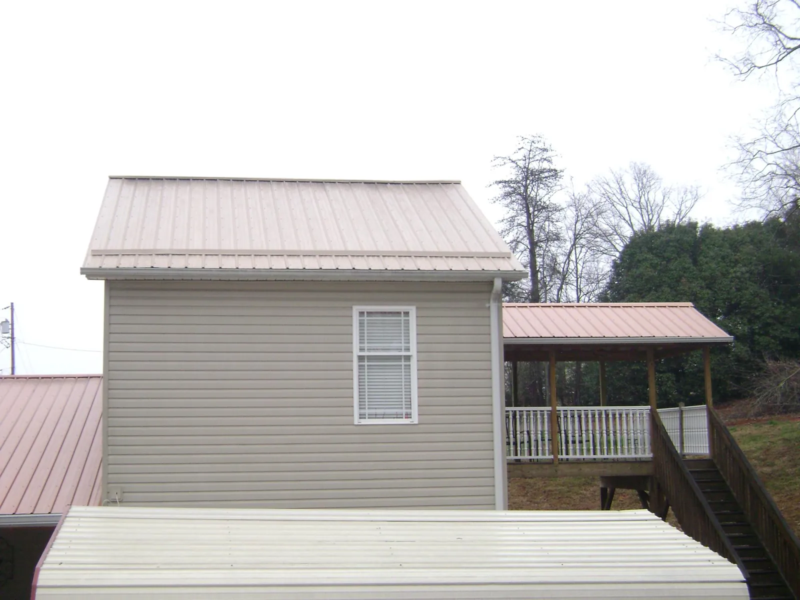 Tan metal roofs on a two story addition and attached porch, from a Roof Replacement job in Laurel